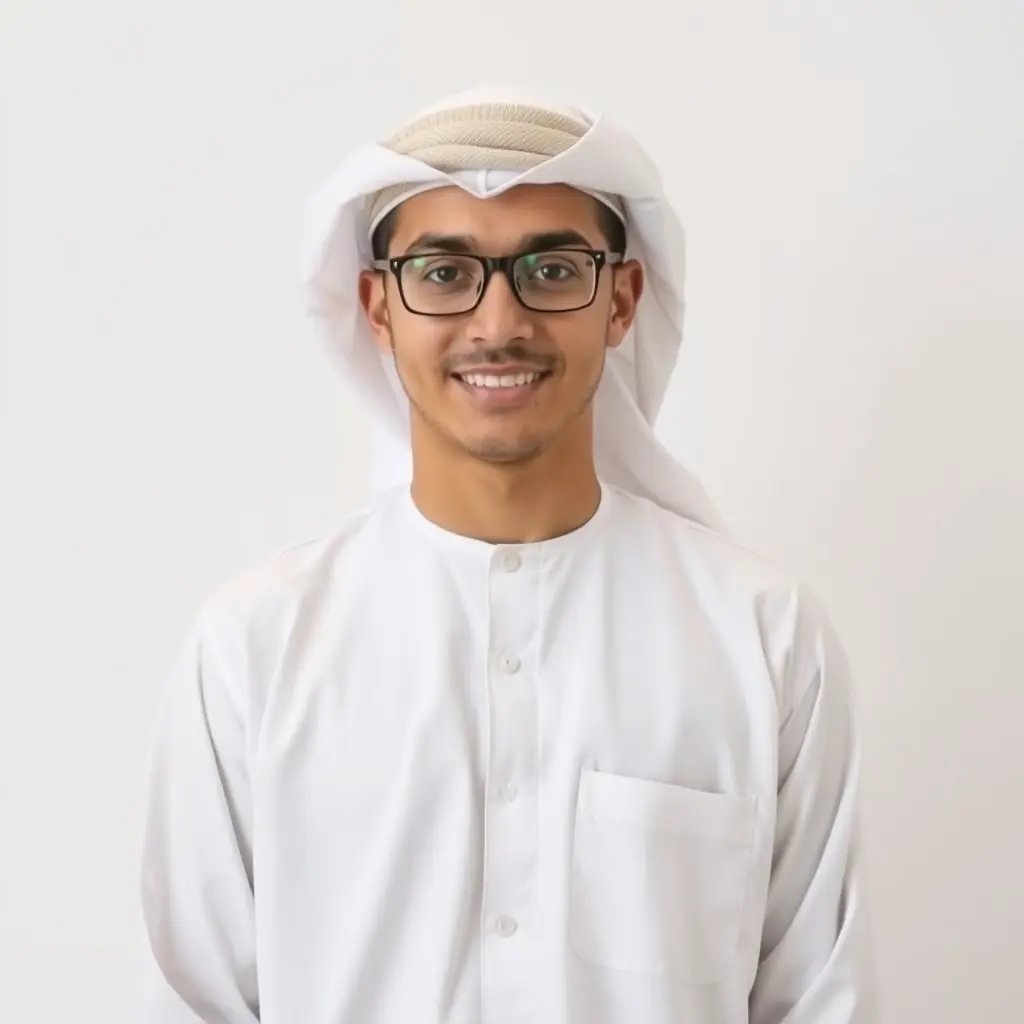 شاب عماني يرتدي الدشداشة التقليدية العمانية ذات اللون الأبيض، ويضع الكوفية العمانية على رأسه بألوان فاتحة جميلة ومتناسقة. يقف بابتسامة بسيطة، تعكس ثقته وودّه. ويرتدي نظارة طبية